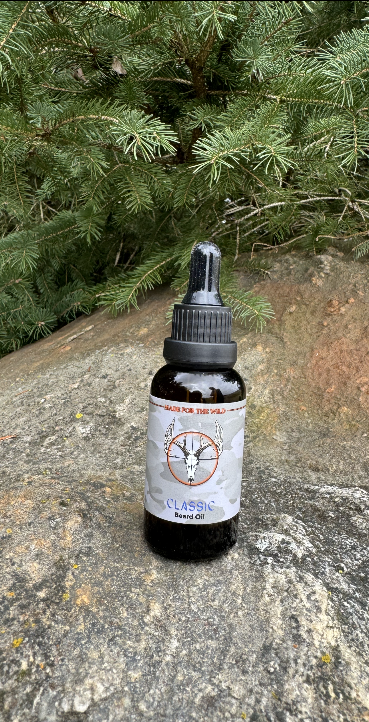 Classic Beard Oil Made for the Wild in Canada. On a rock with a cedar tree branches